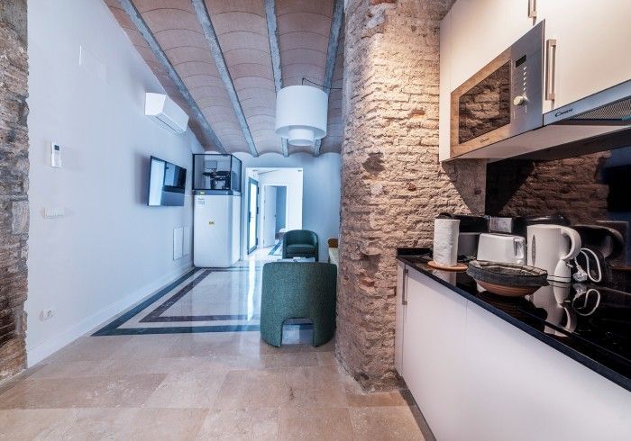 Cocina moderna con pared de ladrillo visto, armarios blancos y encimera negra en un estrecho pasillo de un apartamento.