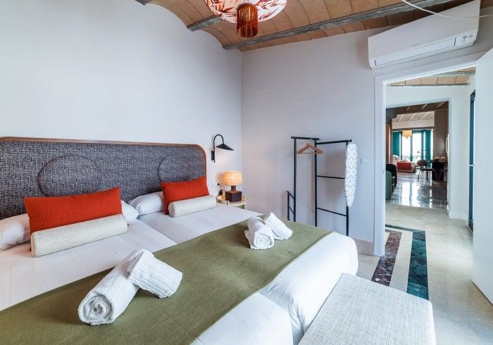 Dormitorio moderno con una cama grande, almohadas naranjas, lámpara de noche y puerta abierta que da a un pasillo.