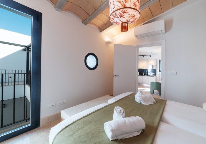Habitación luminosa con cama, puerta de balcón y un pequeño espejo redondo en la pared.