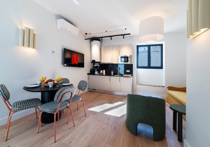 Apartamento moderno de planta abierta con zona de comedor, cocina, sofá y televisor de pared.