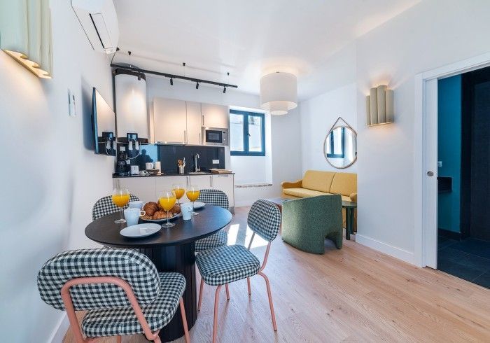 Comedor y cocina modernos y luminosos con mesa redonda, sillas negras y suelos de madera clara.