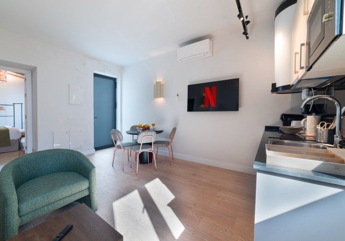 Apartamento tipo estudio moderno con sofá verde, mesa de comedor, cocina y televisor de pared con Netflix.