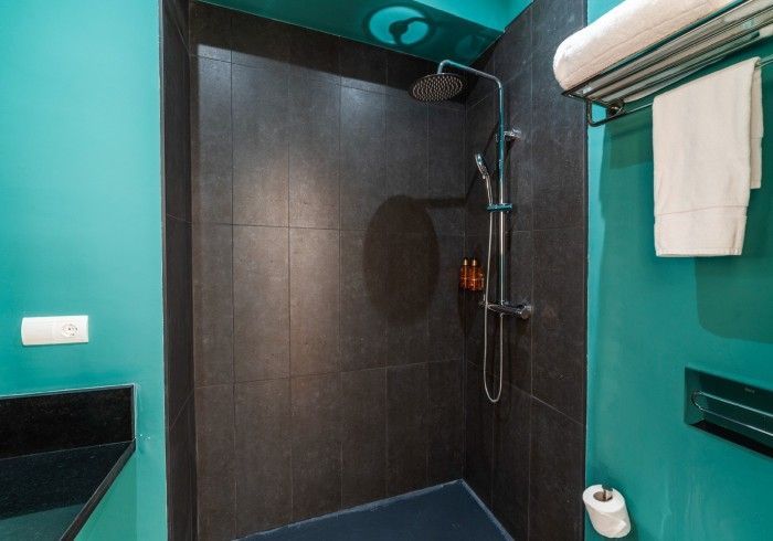 Ducha de baño moderna con azulejos oscuros, paredes color verde azulado y una toalla colgada cerca.