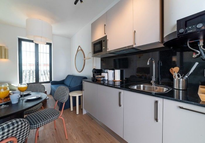 Cocina moderna con armarios blancos, encimeras negras y un pequeño comedor junto a la ventana.