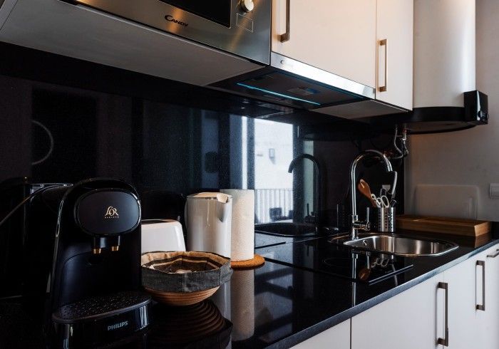 Encimera de cocina moderna en blanco y negro con cafetera, hervidor de agua, fregadero y armarios.