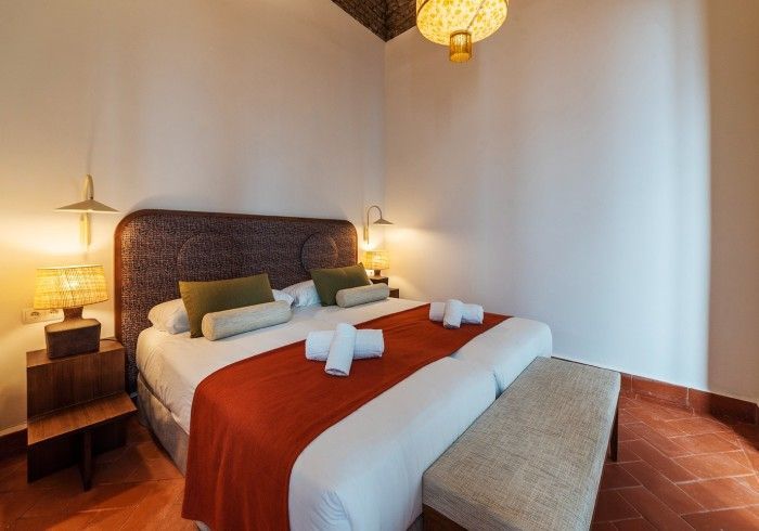 Habitación acogedora con una cama grande, una manta roja, lámparas de noche y un banco a los pies de la cama.