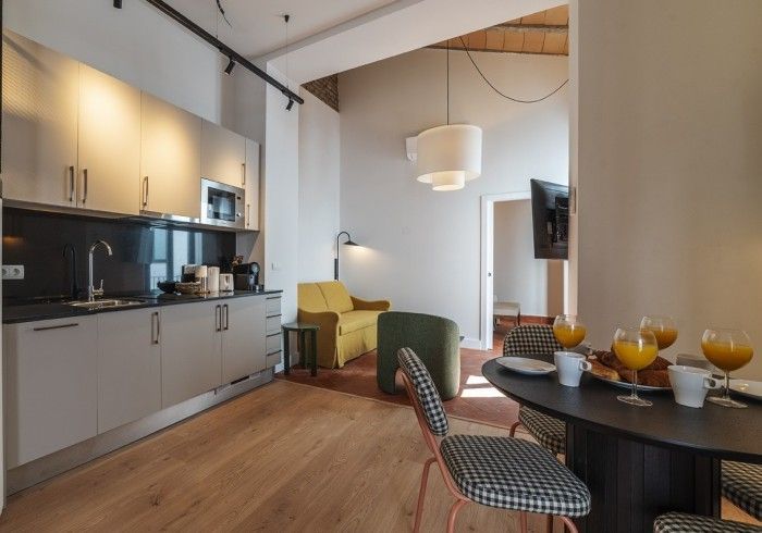 Cocina y comedor modernos de planta abierta con armarios grises, suelo de madera, silla verde y mesa puesta con bebidas.