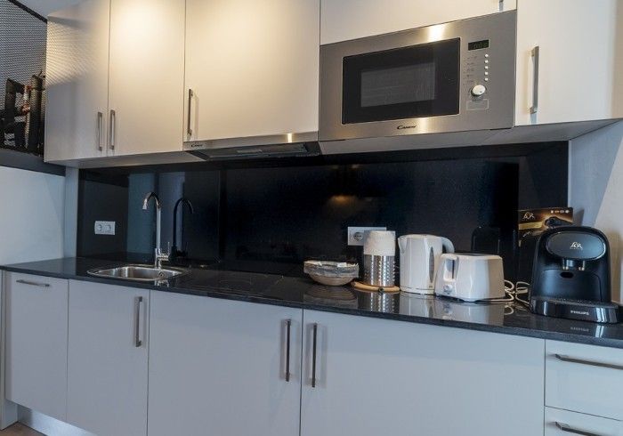 Cocina moderna con armarios blancos, encimera negra, microondas, cafetera y hervidor de agua.