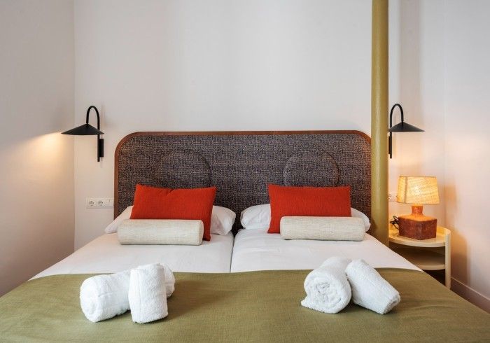 Dormitorio moderno con cabecero tejido, dos almohadas rojas, ropa de cama blanca y lámparas de noche.