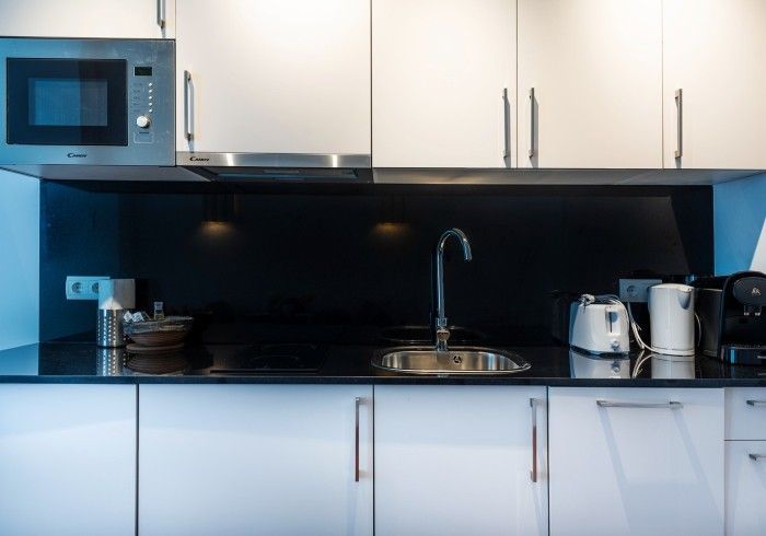 Cocina moderna con gabinetes blancos, protector contra salpicaduras negro, microondas, fregadero y electrodomésticos.