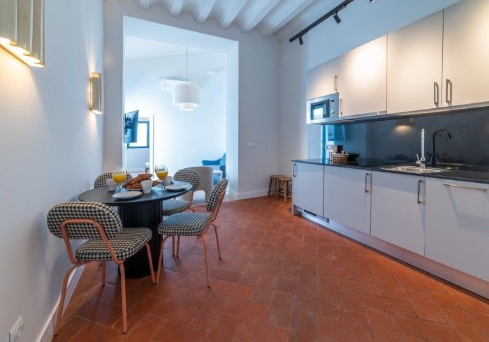 Cocina-comedor moderna con armarios blancos, suelo de terracota y una mesa redonda puesta para comer.