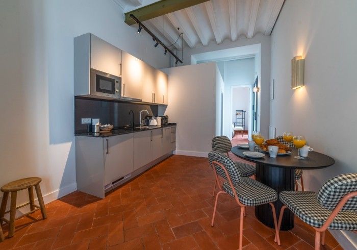 Cocina moderna con rincón de comedor, suelo de terracota, armarios grises y una mesa redonda con fruta.