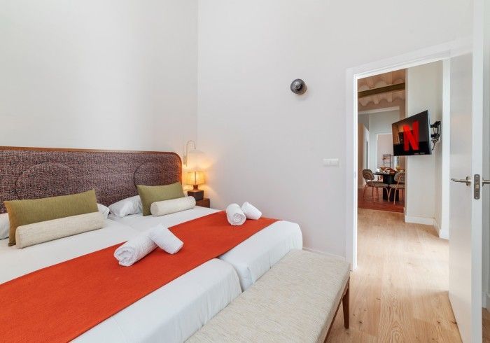 Habitación luminosa con colcha naranja, toallas blancas y una puerta abierta que da a una sala de estar.