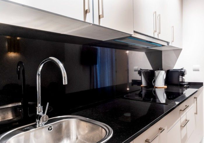 Encimera de cocina moderna con fregadero de acero inoxidable, protector contra salpicaduras negro, gabinetes blancos.