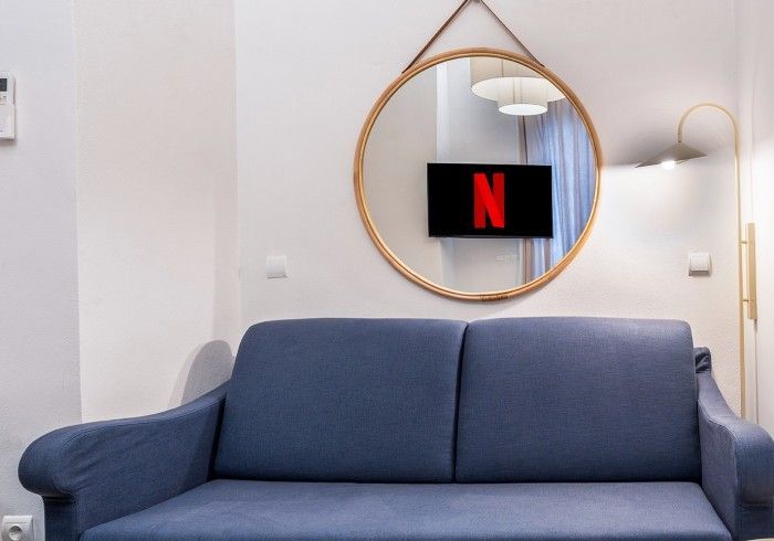 Sofá azul en una habitación moderna con un espejo redondo que refleja un televisor que muestra el logotipo de Netflix.