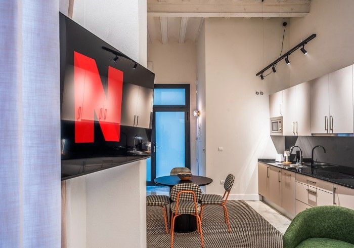 Sala de estar de apartamento moderno con televisor montado en la pared, mesa de comedor y área de cocina.