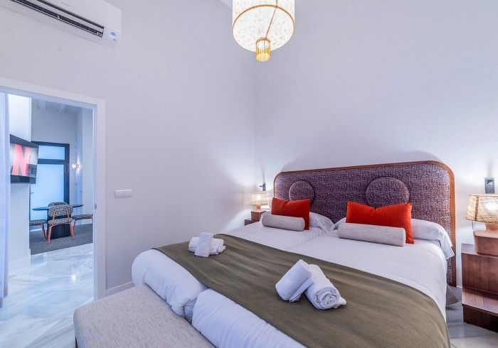 Dormitorio luminoso con paredes blancas, cabecero estampado, ropa de cama verde y puerta que da a una habitación.