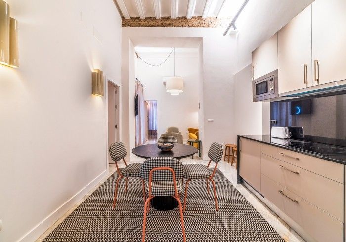 Cocina moderna con gabinetes blancos, detalles de madera, piso estampado y una pequeña mesa de comedor con sillas.
