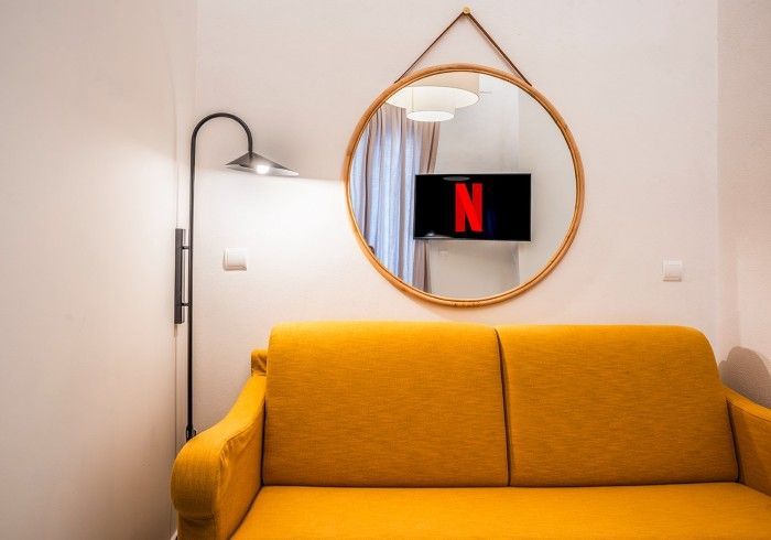 Sofá amarillo en una habitación moderna con una lámpara de pared y un espejo redondo que refleja una pantalla de televisión.