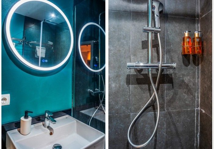 Baño moderno con espejo redondo iluminado, lavabo blanco, pared color turquesa y ducha de cristal con grifería cromada.