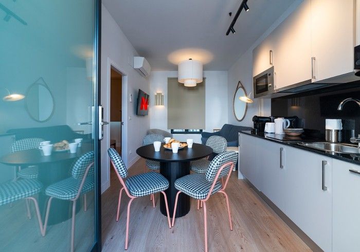 Cocina moderna con mesa de comedor negra, sillas estampadas, armarios blancos y una pared de cristal a la izquierda.