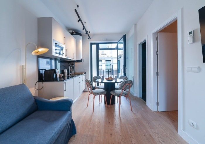Apartamento luminoso y moderno con sofá azul, cocina, mesa de comedor y un amplio balcón con ventanal con vistas.