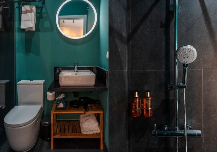 Baño moderno con paredes color turquesa, espejo redondo, inodoro blanco, lavabo, ducha y artículos de tocador de cobre.