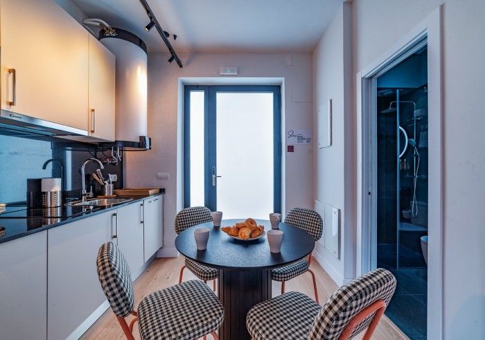 Pequeña cocina con mesa de comedor redonda, cuatro sillas y una luminosa puerta de cristal que da al exterior.