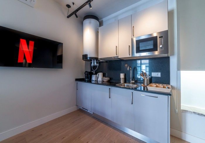 Cocina moderna con armarios grises, microondas, cafetera y televisor de pared con el logotipo de Netflix.