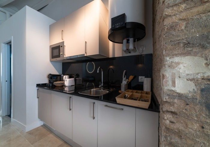 Encimera de cocina moderna con gabinetes blancos, salpicadero negro, fregadero, estufa, microondas y detalle de pared.