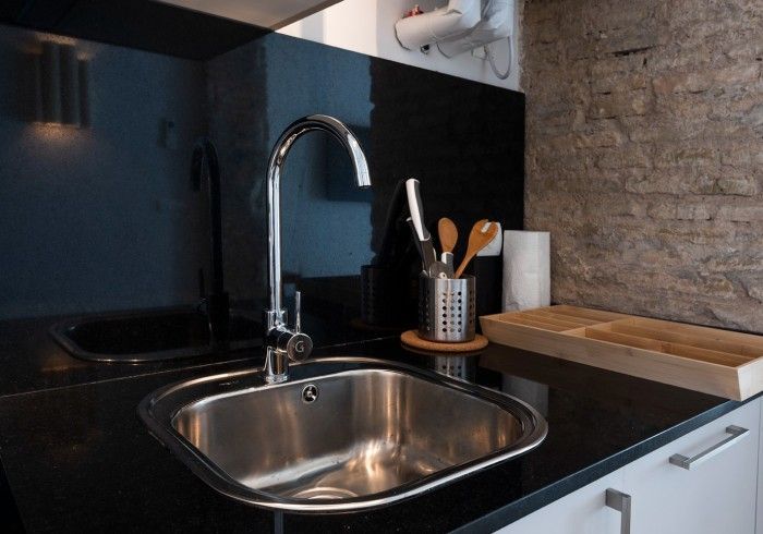 Fregadero de cocina moderno con grifo cromado, protector contra salpicaduras negro y tabla de cortar de madera.
