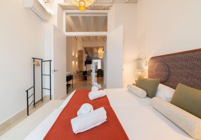 Habitación de hotel luminosa con cama king size, alfombra roja y vistas a un pasillo y a la sala de estar.