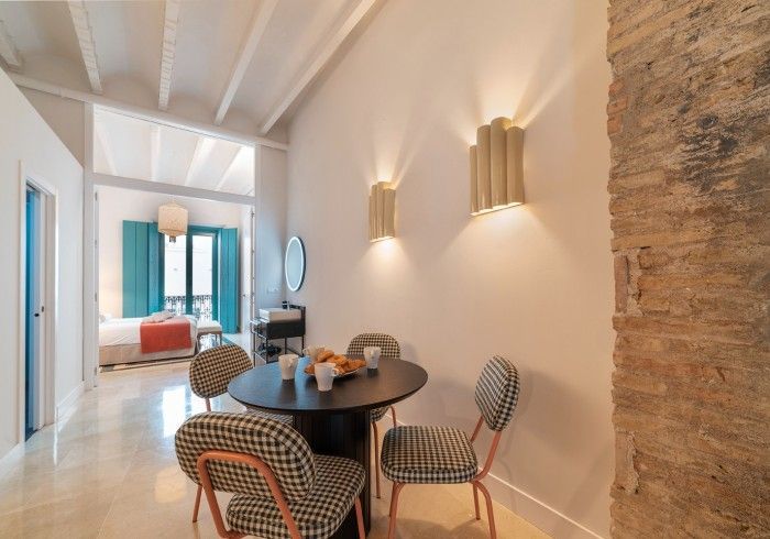 Luminoso comedor en el pasillo con mesa redonda, sillas estampadas, apliques de pared y una pared decorativa de piedra.