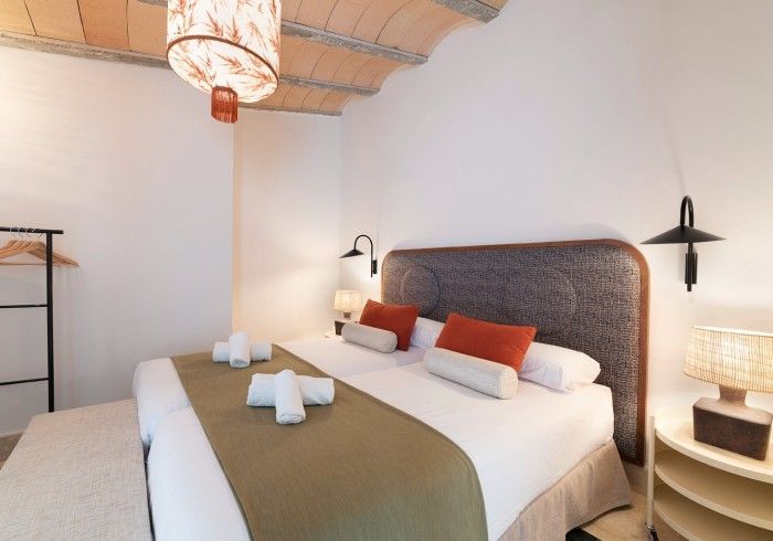 Dormitorio moderno con cama blanca, manta verde, almohadas naranjas y lámpara colgante tejida.