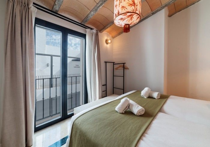 Habitación luminosa con cama king size, manta verde, puertas que dan al balcón y lámpara colgante tipo farol.