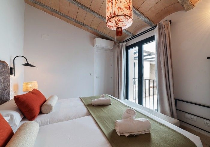 Acogedora habitación con dos camas individuales, paredes blancas, techo de madera y puerta con balcón y ventana.