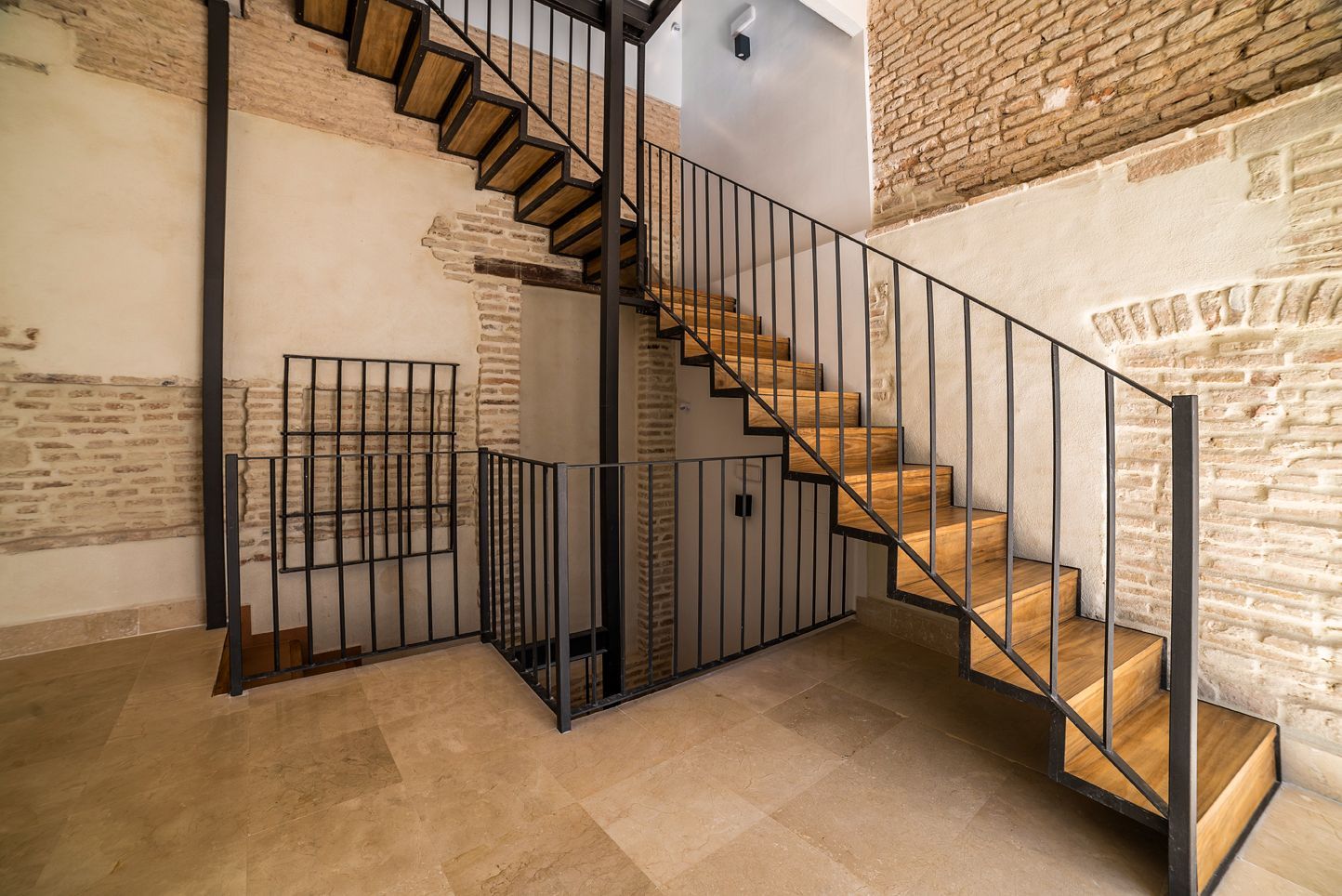 Escalera interior con barandilla de metal negro en una habitación de ladrillo y piedra.