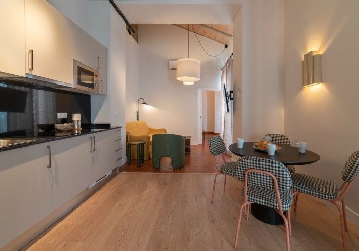 Moderna zona de cocina y comedor con armarios blancos, suelos de madera, mesa redonda y sillas estampadas.