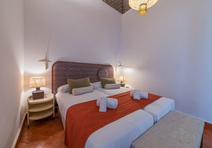 Habitación acogedora con cama, manta naranja, lámparas de noche y lámpara colgante tejida.