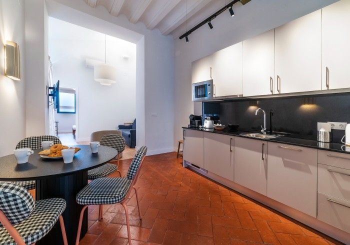 Cocina moderna y luminosa con armarios blancos, salpicadero negro y una mesa de comedor redonda sobre un suelo de baldosas.