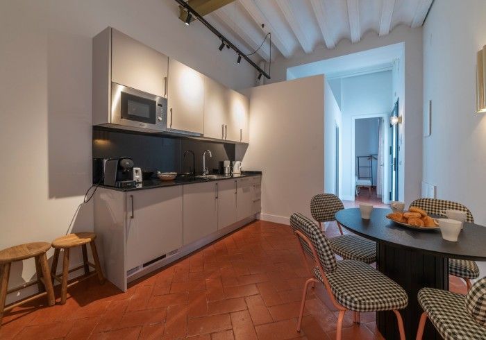 Cocina-comedor moderna con armarios grises, suelo de terracota y mesa redonda con sillas estampadas.