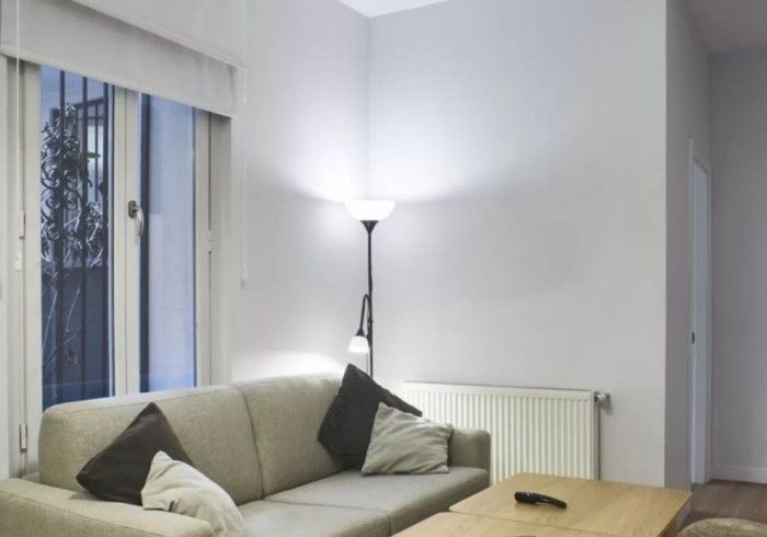 Sala de estar luminosa con sofá beige, lámpara de pie, radiador y cortinas en la ventana.