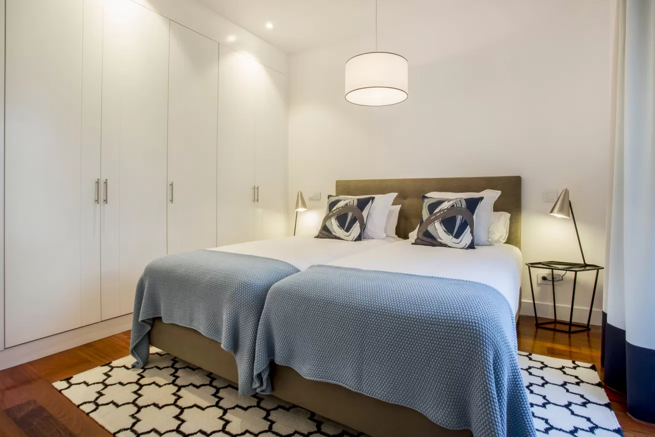 Habitación luminosa y moderna con cama de matrimonio, armarios empotrados blancos y alfombra estampada en blanco y negro.