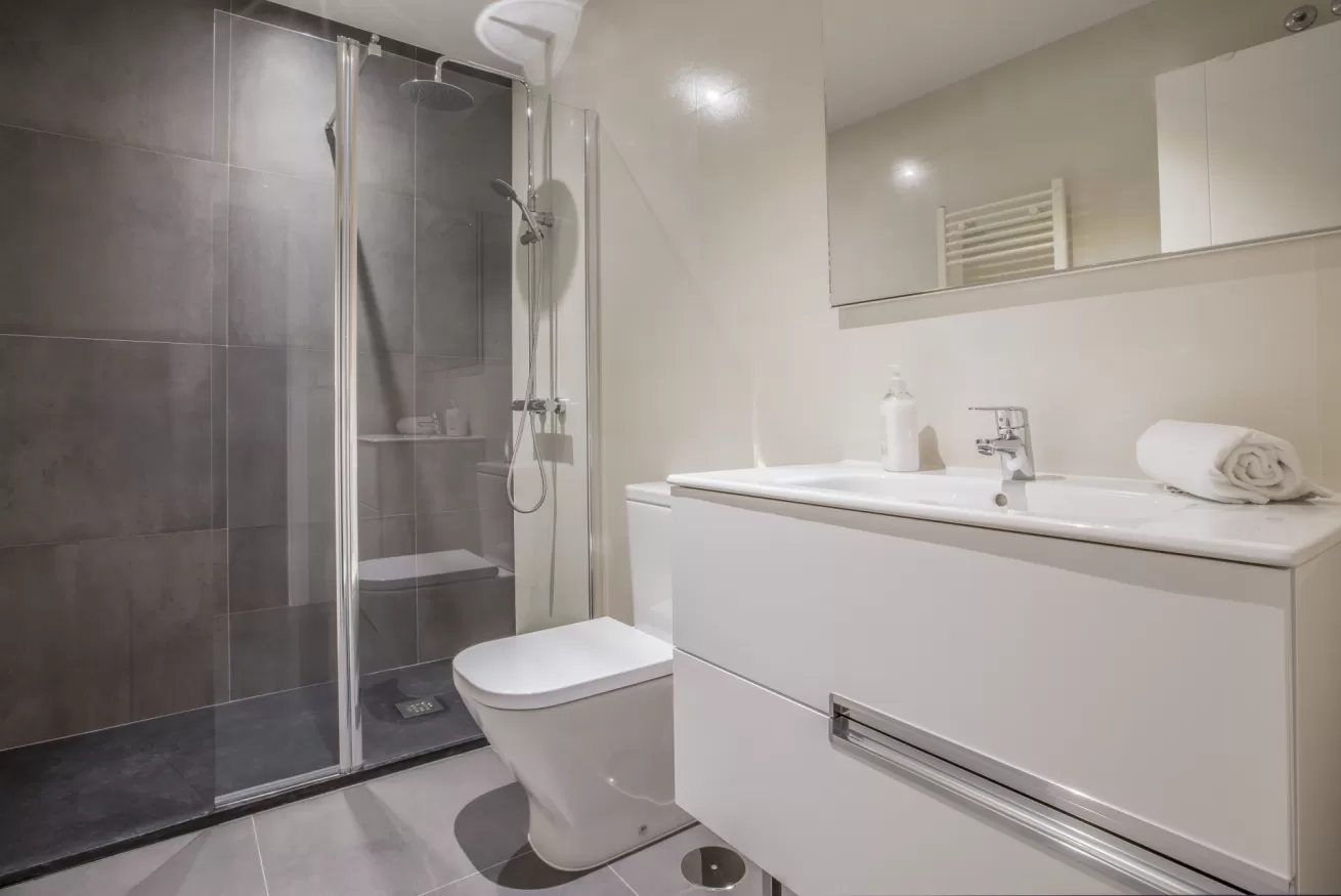 Baño moderno con ducha de cristal, inodoro y lavabo blanco.