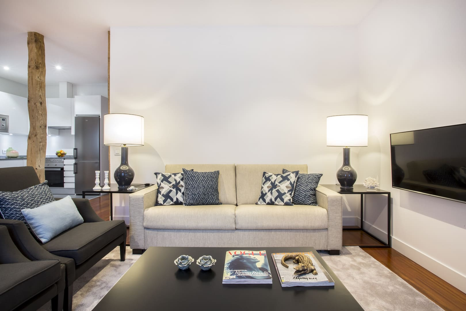 Sala de estar moderna con sofá blanco, mesa de centro negra, lámparas, alfombra gris y televisor montado en la pared.