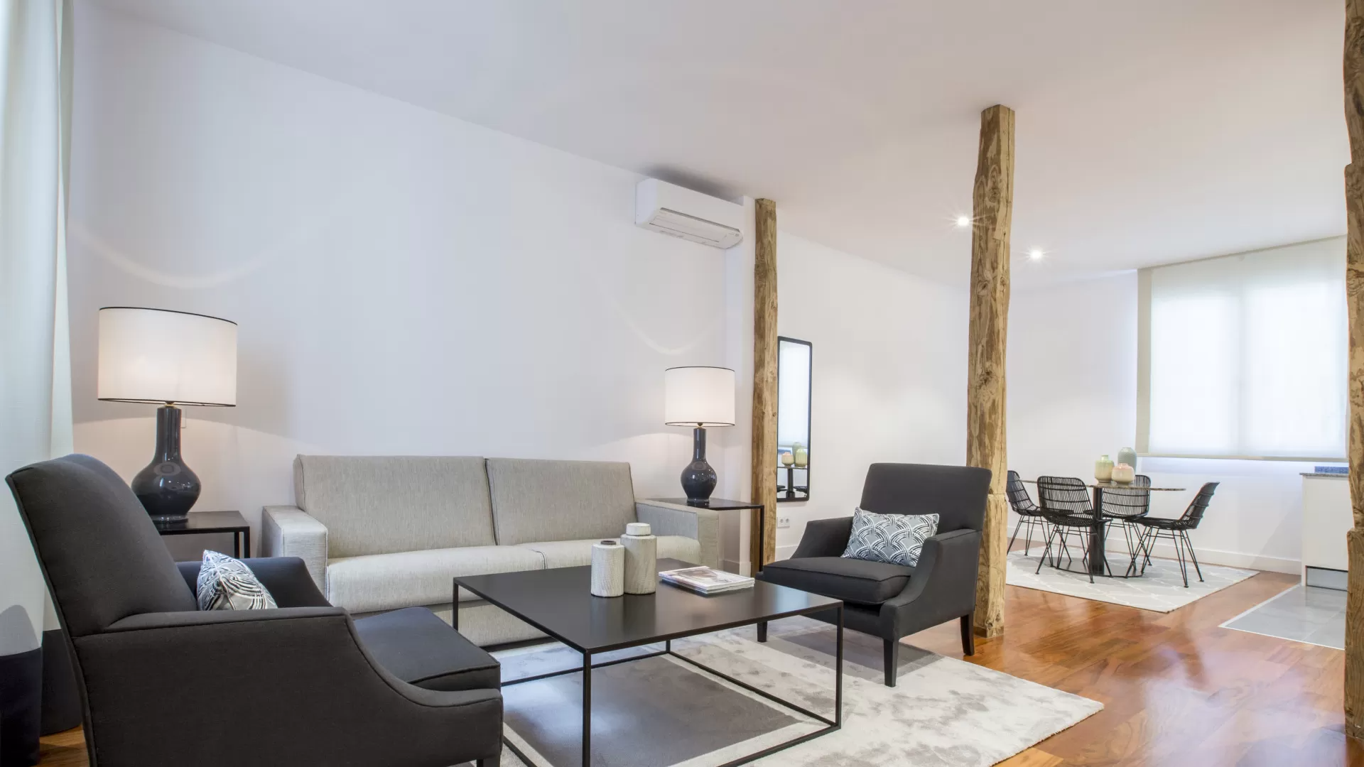 Sala de estar moderna y luminosa con sofá blanco, sillones oscuros, mesa de centro y zona de comedor abierta.