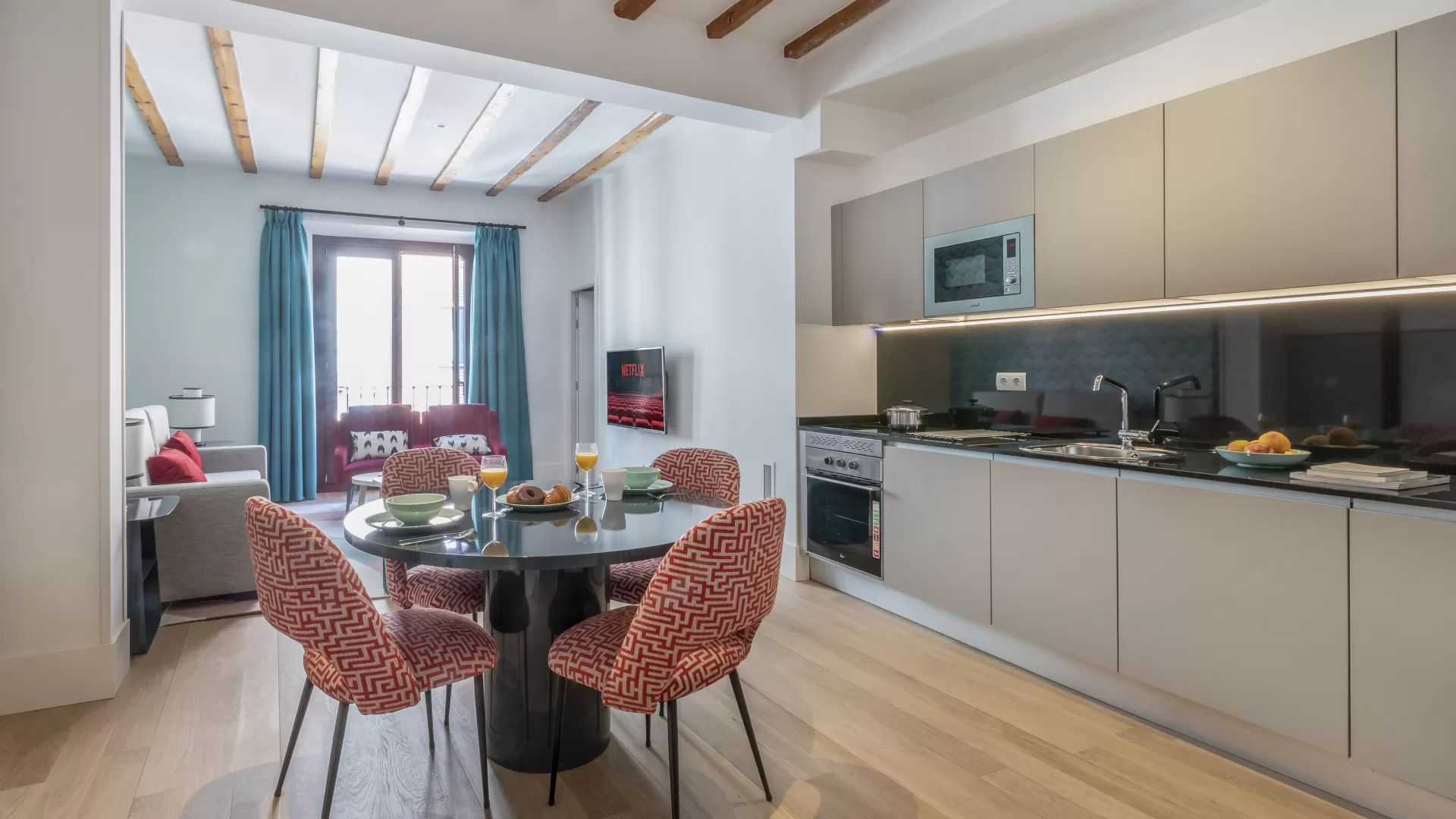Cocina-comedor moderna con mesa redonda, sillas estampadas y armarios beige.