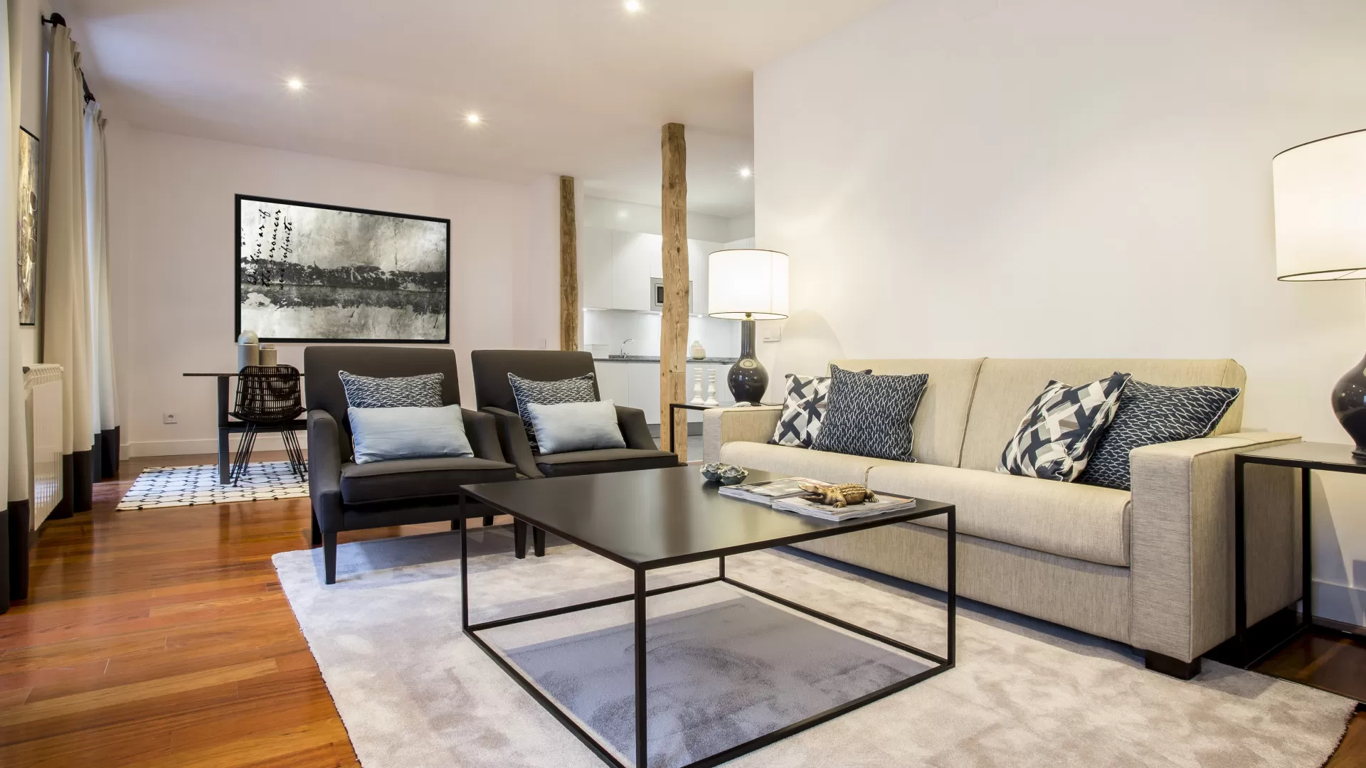 Sala de estar moderna con sofá beige, sillas oscuras, mesa de centro y lámpara de pie sobre suelo de madera noble.