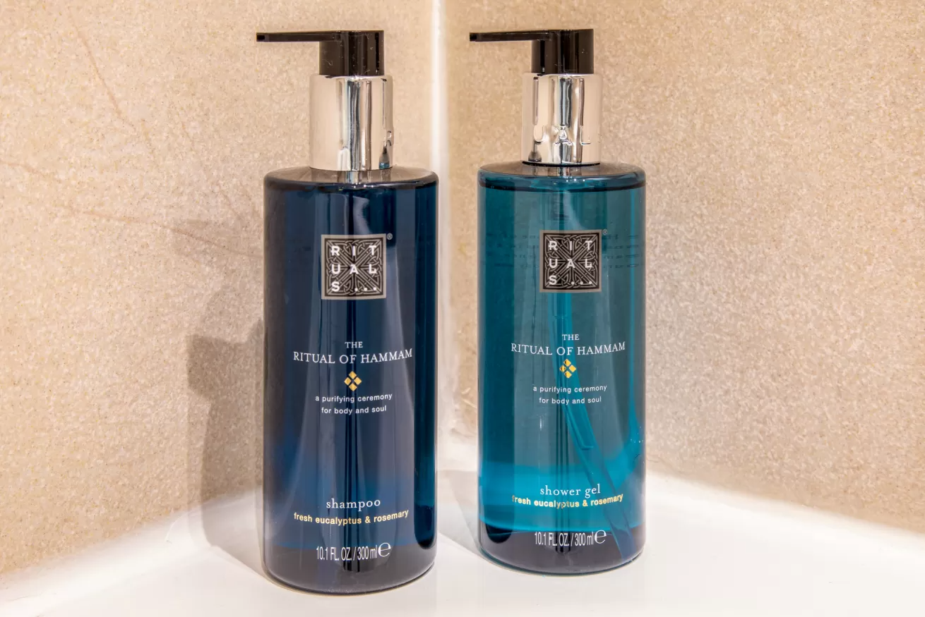 Dos dispensadores de jabón líquido azules con bombas negras sobre un mostrador de baño contra una pared beige.