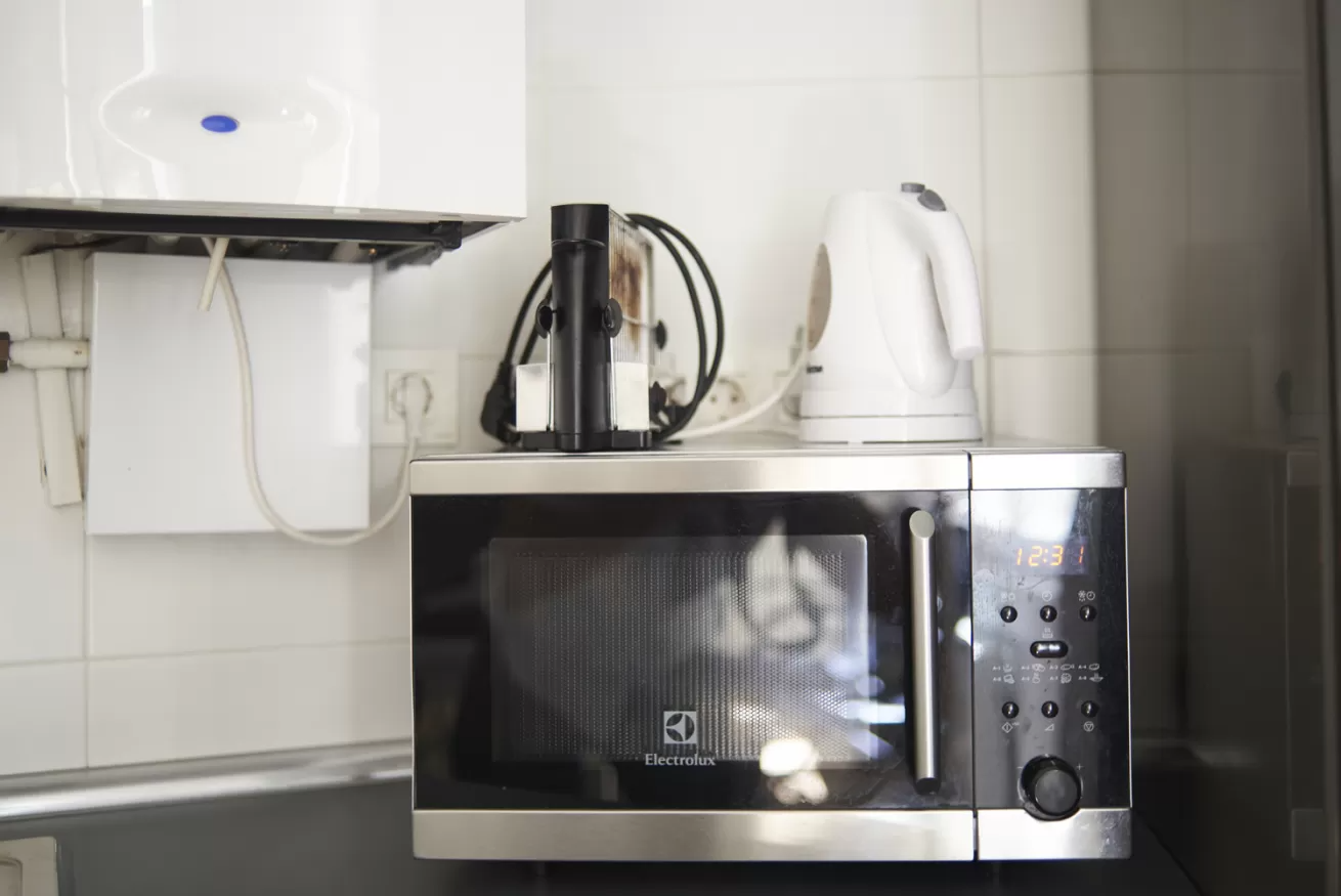 Encimera de cocina con microondas de acero inoxidable, hervidor eléctrico y hervidor de agua bajo armarios blancos.